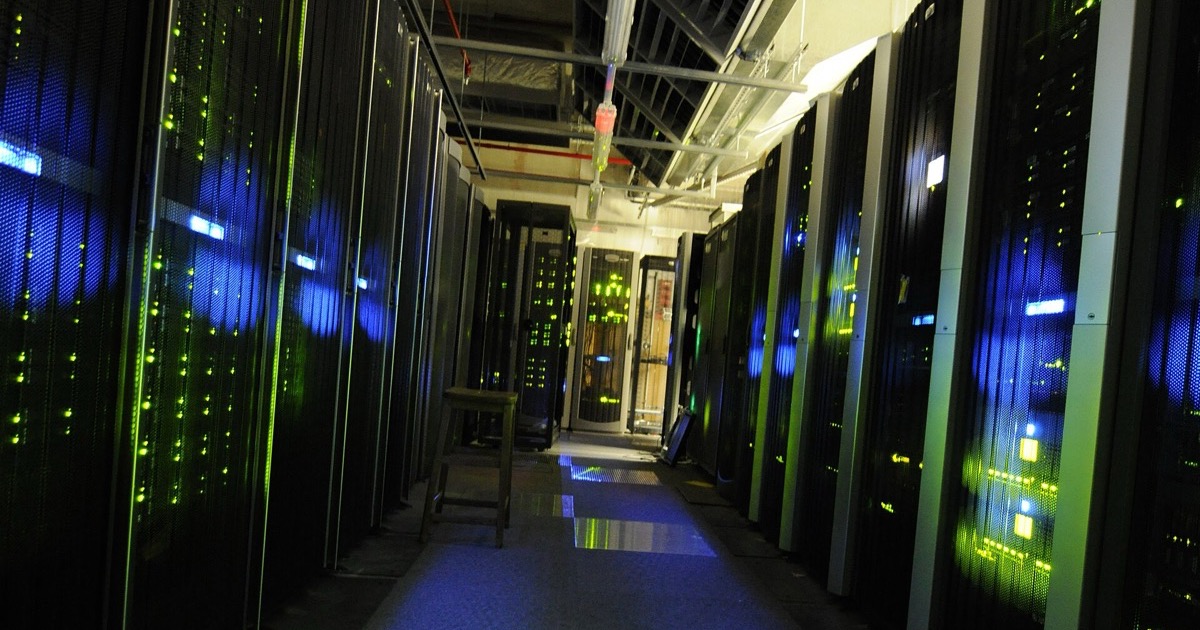 A data-center server room aisle lined with racks glowing green and blue, symbolizing the AI infrastructure demand behind Micron's blowout earnings on June 24, 2026.