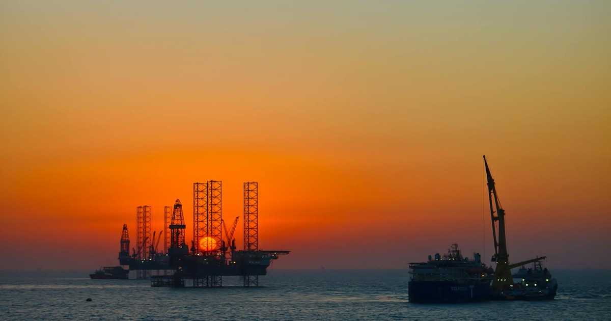 Offshore oil rig and supply ship silhouetted against a vibrant sunset over the ocean