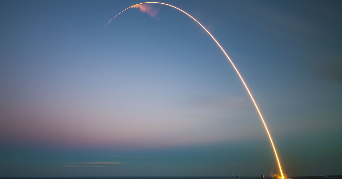 SpaceX rocket launch light trail streaking across the dusk sky over water at Cape Canaveral