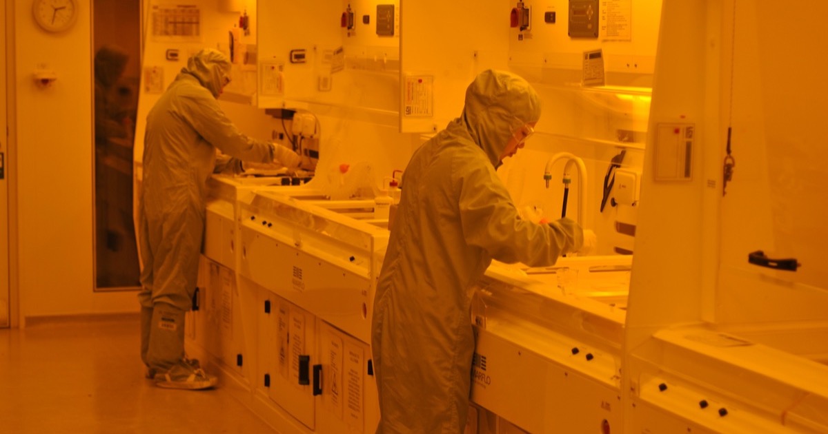 An orange-lit semiconductor photolithography cleanroom where chips are patterned at nanometer scale, illustrating IBM's sub-1nm angstrom-era breakthrough.