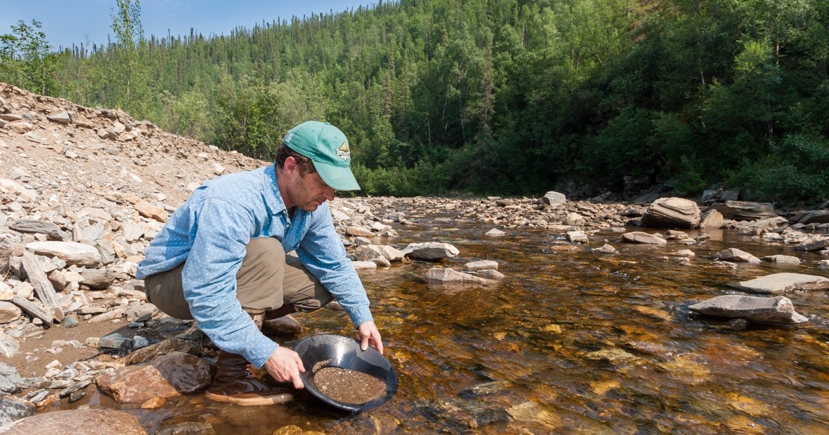 A prospector crouched in a creek panning gravel for gold — factor mining keeps grams of signal from tons of data