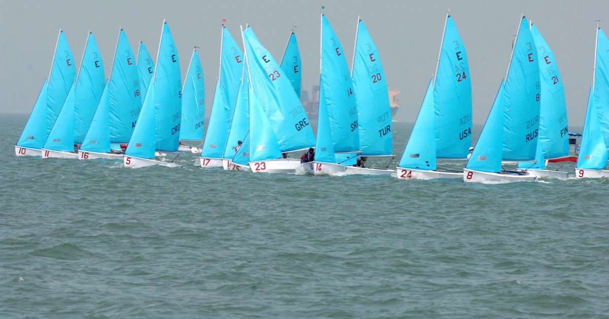 A fleet of identical numbered sailing dinghies racing in the same wind, some boats ahead of others — relative position is the signal