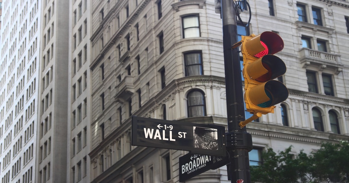 A neoclassical financial district building on Wall Street with traffic lights in the foreground