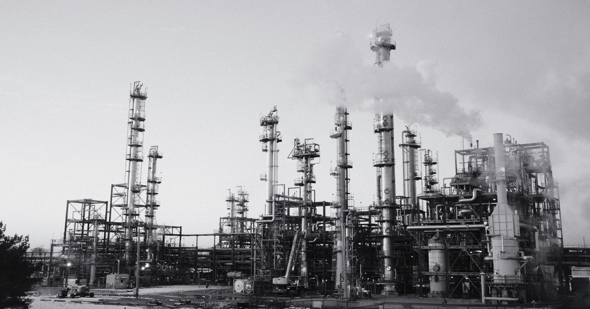 Industrial oil refinery with smoking stacks under a cloudy sky symbolizing the crude oil price surge