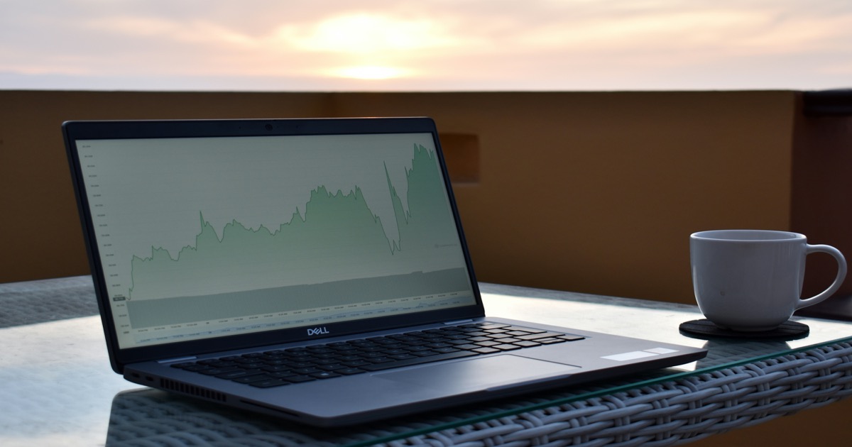 Laptop on a desk with financial market charts in a morning workspace