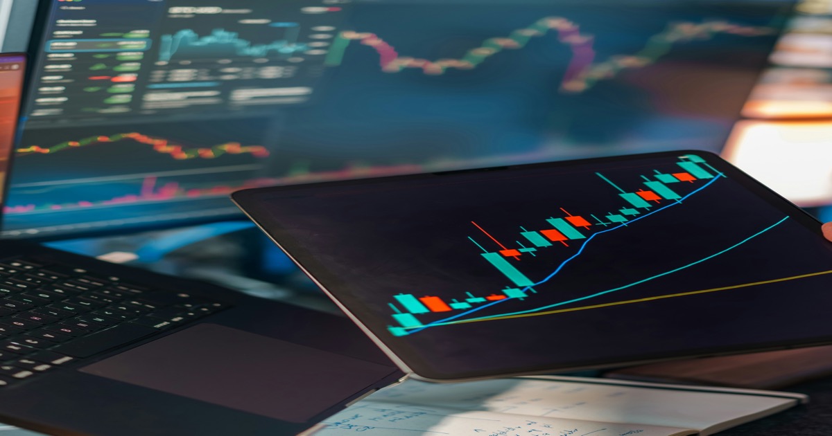 Trading charts displayed across multiple screens and a tablet