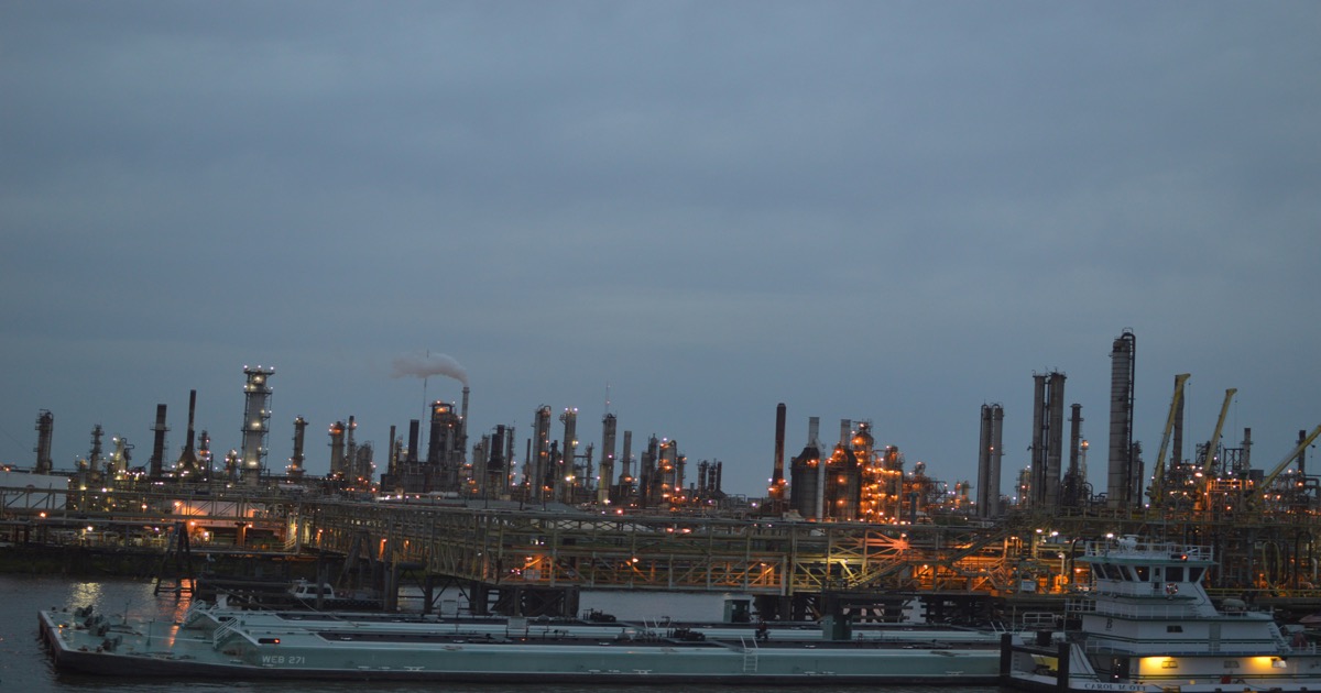 Industrial refinery complex at dusk with barges on the Mississippi River