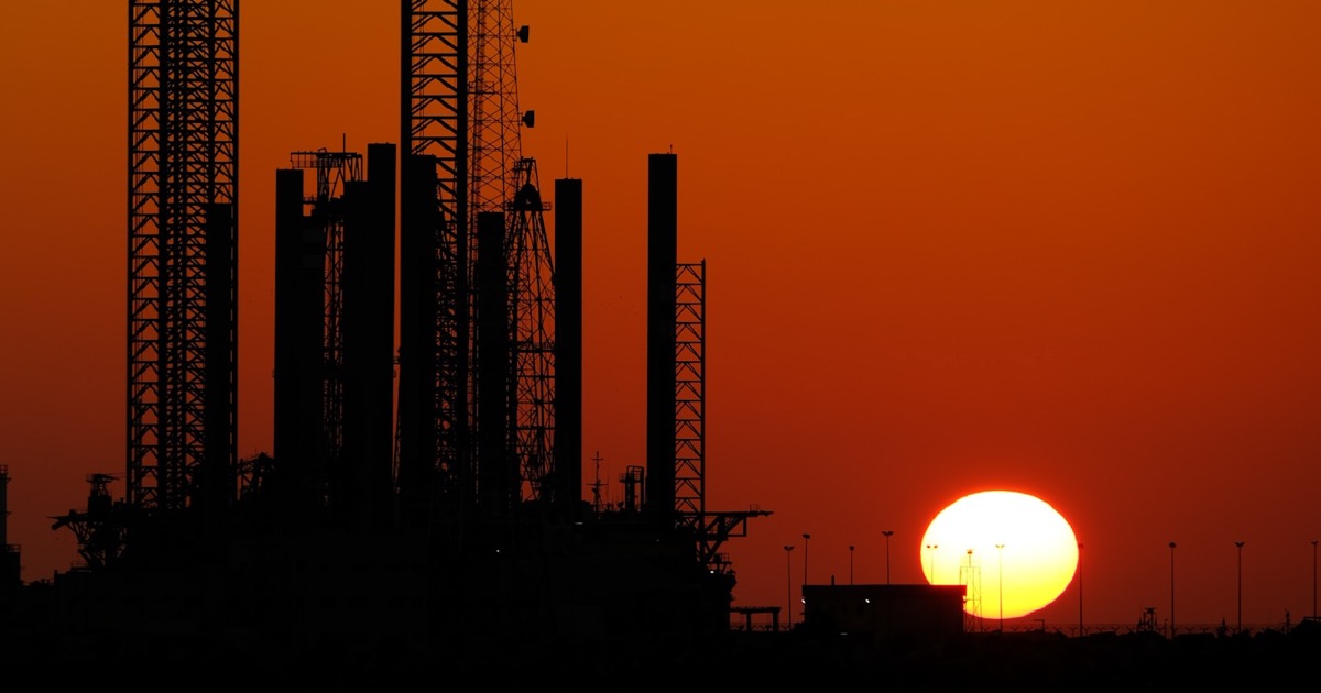 Oil refinery silhouetted against a dramatic orange sunrise, symbolizing crude prices near $100 amid Iran-Hormuz tensions