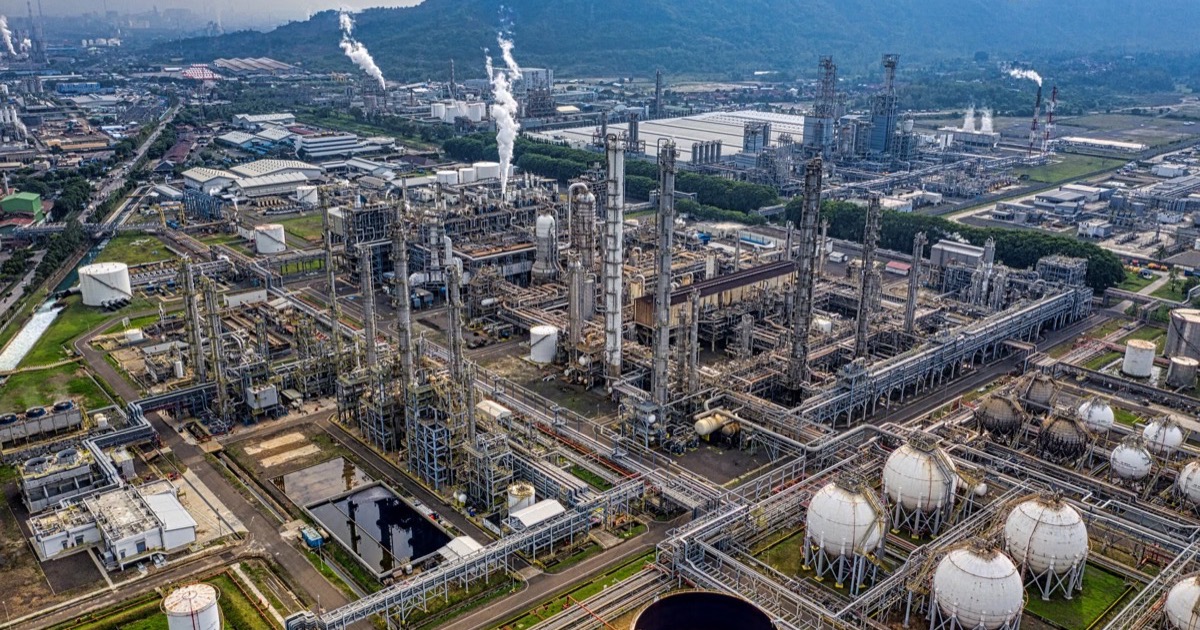 An aerial view of an oil refinery shows storage tanks, towers, and pipelines as crude prices approach $100.