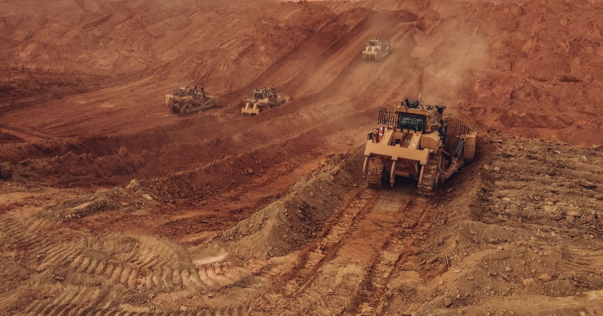 Heavy mining equipment moving red earth in an open-pit mine, representing the scarcity and production economics driving Basic Materials.
