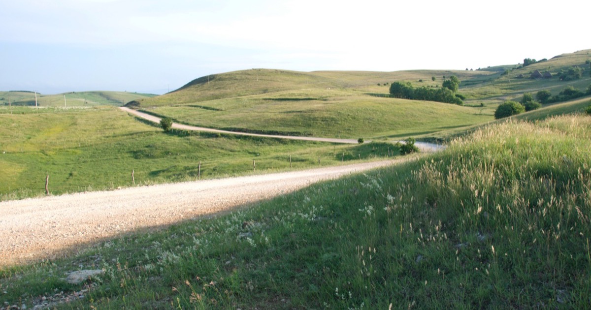 A winding gravel road climbing across a mountain plateau, symbolizing the forward-looking June 29 to July 3, 2026 market road ahead for the AlphaEdge Week Ahead Outlook.